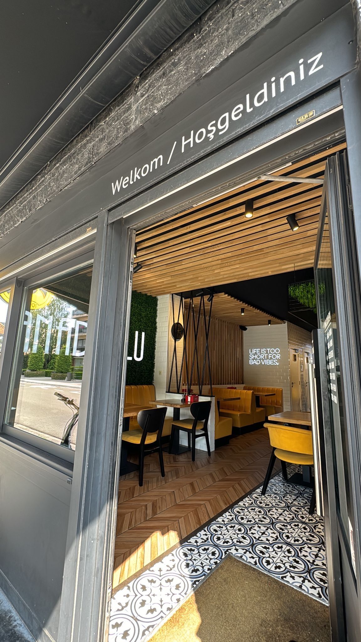 De open gevel van Anadolu take-away in Sint-Niklaas, met "Welkom / Hoşgeldiniz" boven de ingang en gele zitbanken binnen
